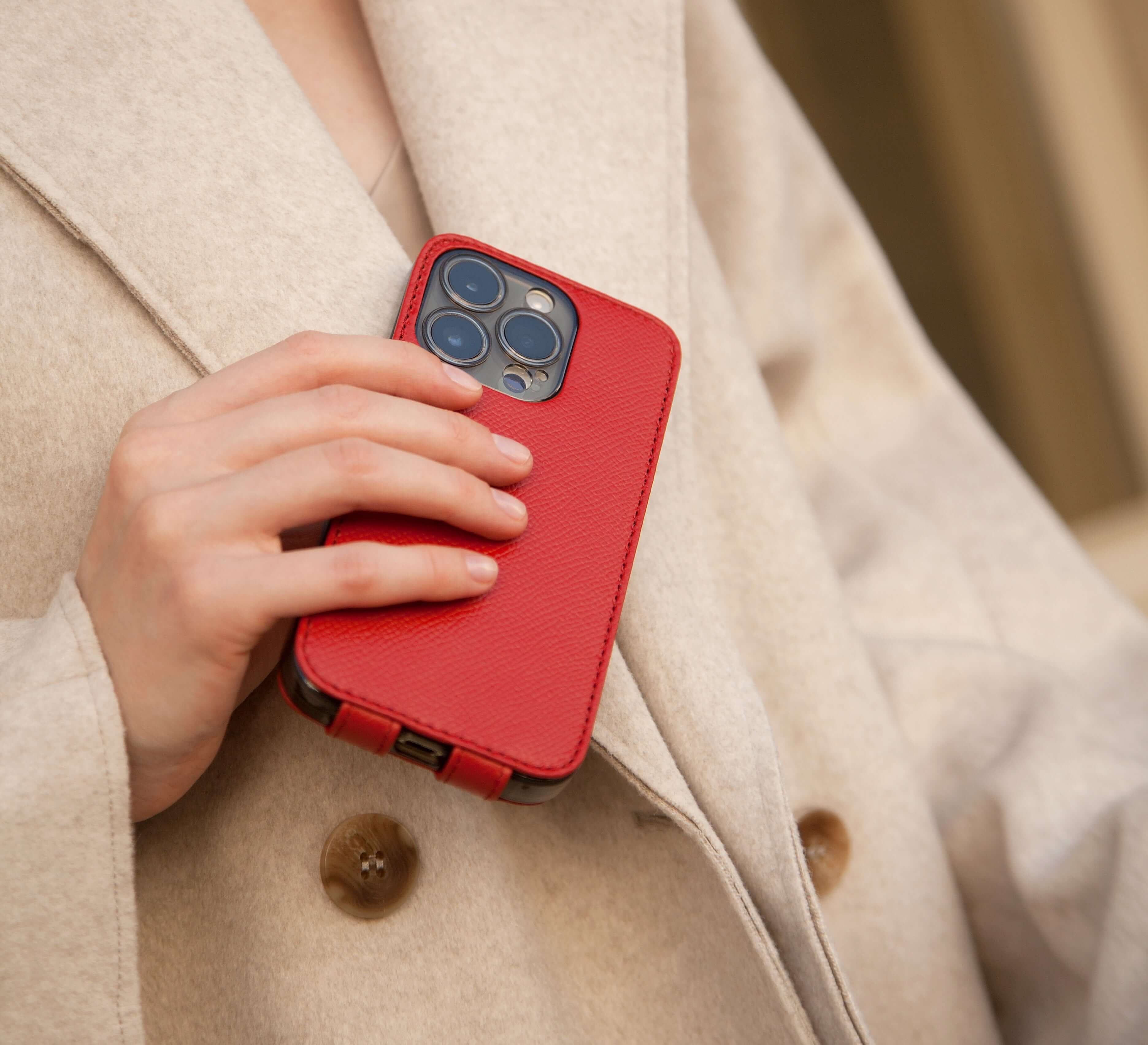 Person holding a phone in red leather flip case, wearing a beige coat.