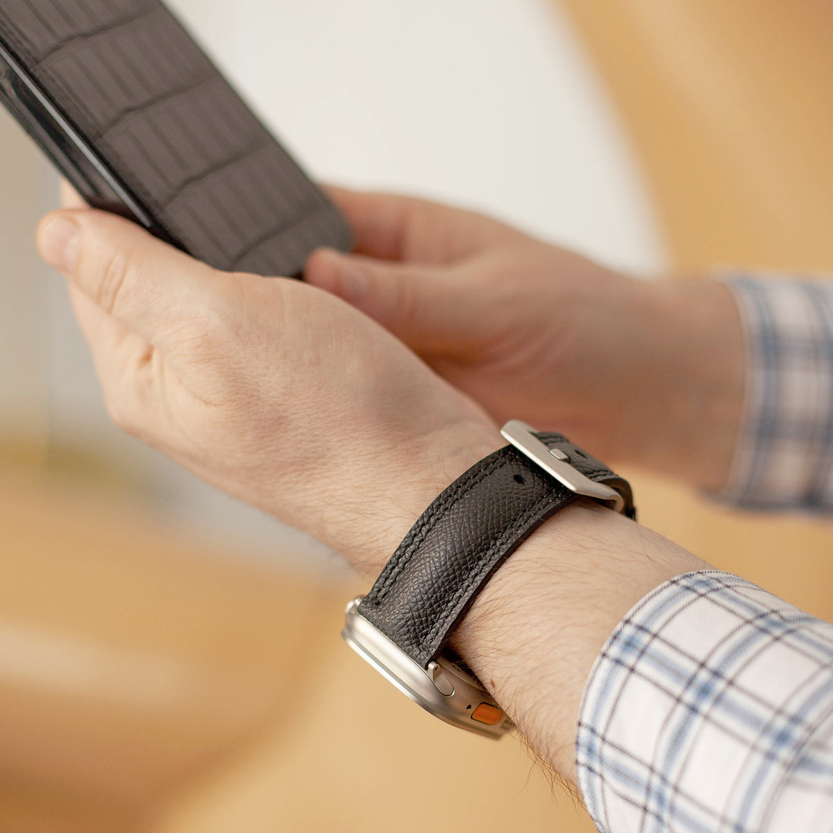 Apple Watch Ultra bandje heren 49 mm zwart Epsom leer om de pols gedragen, titanium gesp, met een leren telefoonhoesje in de hand