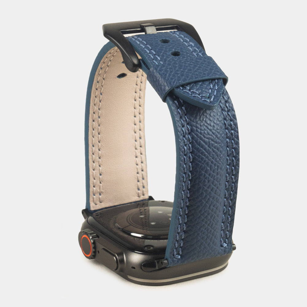 Apple Watch Ultra bandje heren 49 mm blauw Epsom leer met zwarte gespen — verhoogd driekwart achteraanzicht op de zwarte kast, crèmekleurige Alsavel voering en geverfde rand