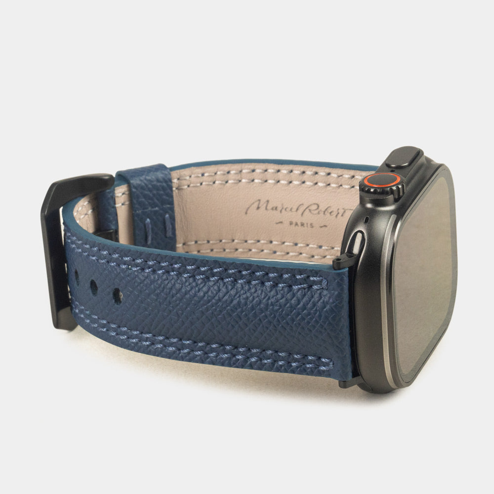 Apple Watch Ultra bandje heren 49 mm blauw Epsom leer met zwarte gespen — driekwart profiel op de zwarte Ultra-kast, crèmekleurige Alsavel voering met stempel Marcel Robert Paris