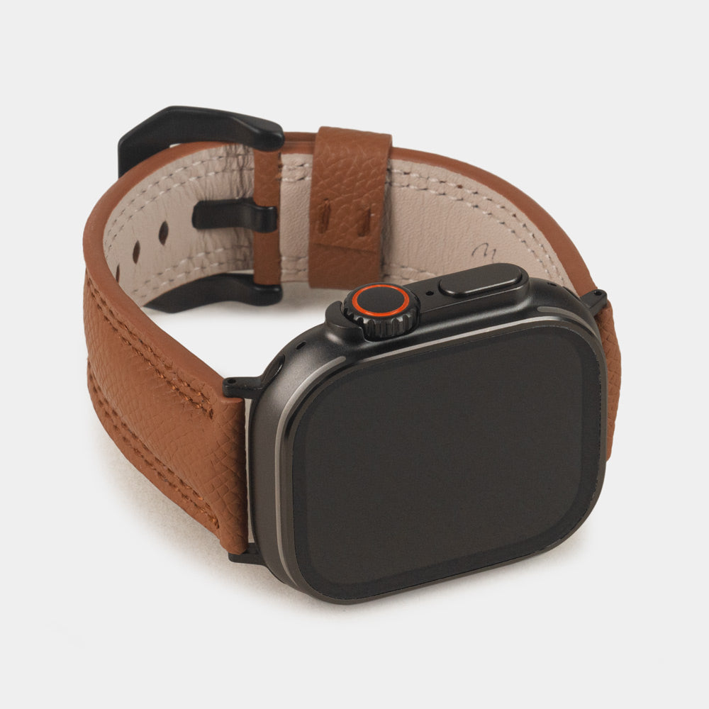 Apple Watch Ultra bandje heren 49 mm goud Epsom leer met zwarte gespen — driekwart profiel op de zwarte Ultra-kast, crèmekleurige Alsavel voering met stempel Marcel Robert Paris