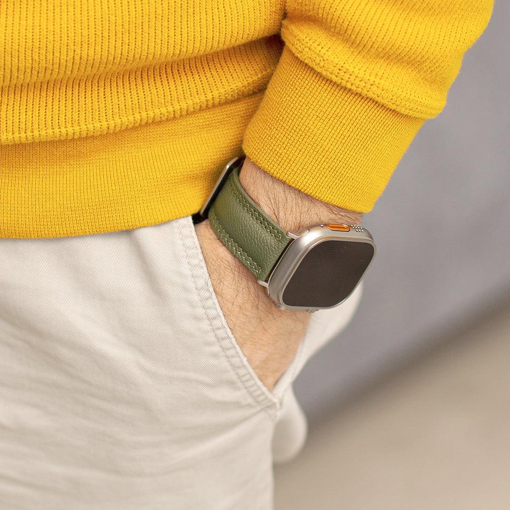 Apple Watch Ultra bandje heren 49 mm kakigroen Epsom leer om de pols gedragen met een gele trui, hand in de zak