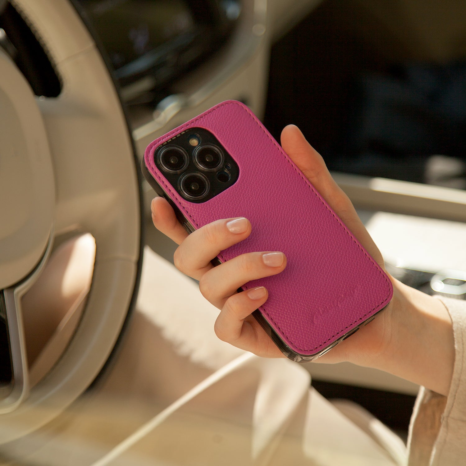 Hand holding iPhone 15 with Marcel Robert fuchsia calfskin leather case back view showing grained texture