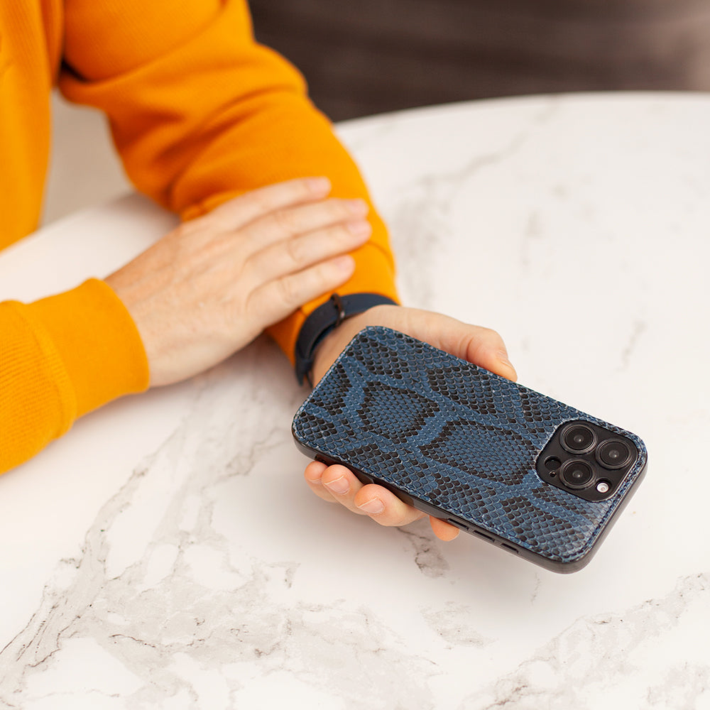 Person holding a phone with a blue snake-textured case on a marble surface