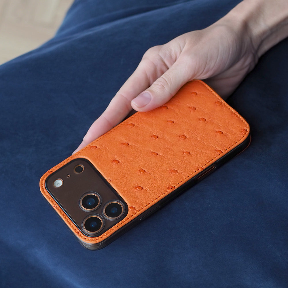 iPhone 17 Pro & Pro Max cover case in orange ostrich leather – held in hand, showing the ostrich quill pattern and the camera cut-out