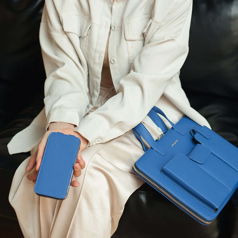 Person holding a phone in blue leather case and blue handbag