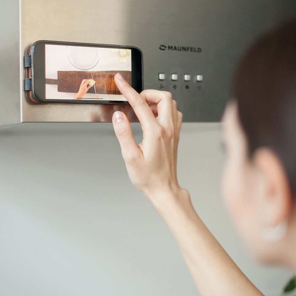 Person using a smartphone in leather made case with magnets on a kitchen appliance, likely a microwave.