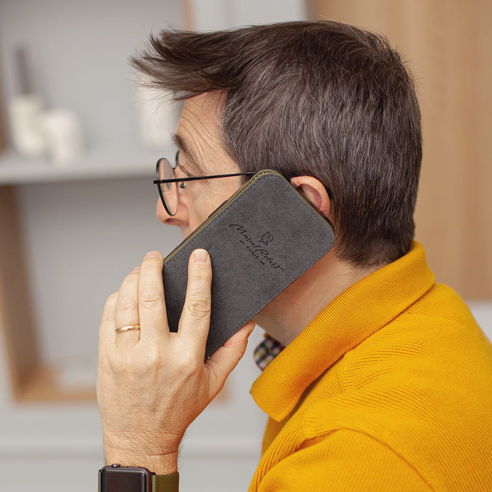 Person holding a phone in leather case with a brand logo, wearing a yellow shirt.