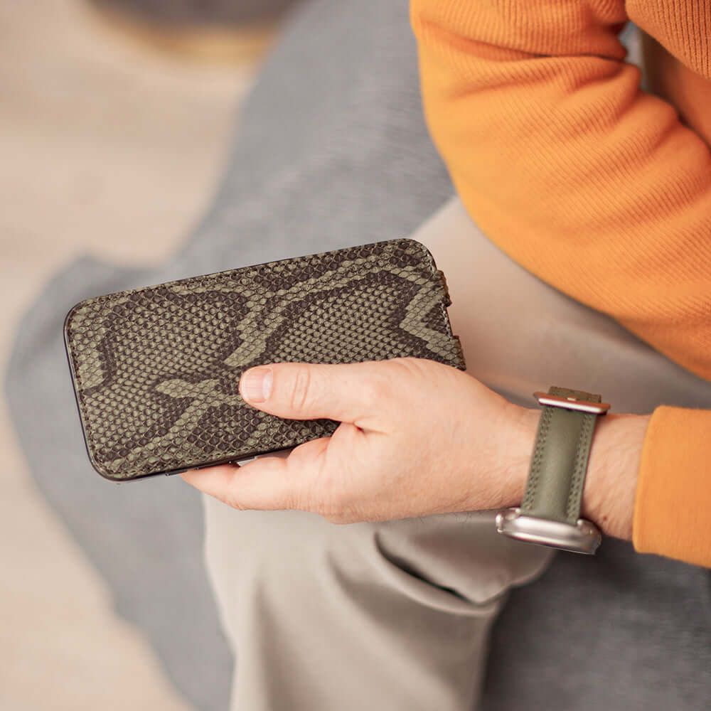 Person holding iphone in python leather case with a watch on the wrist, wearing an orange sweater