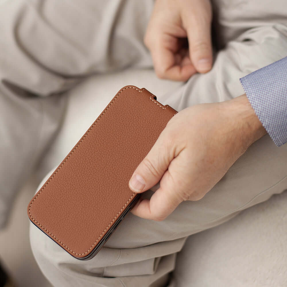 Person holding a smartphone with a brown leather case against a neutral background