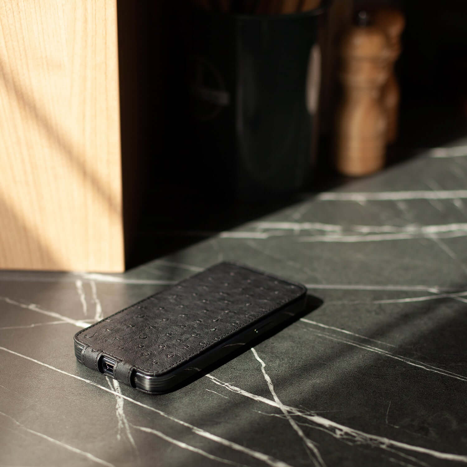 Black phone in case made of black ostrich leather on a marble surface with a blurred background