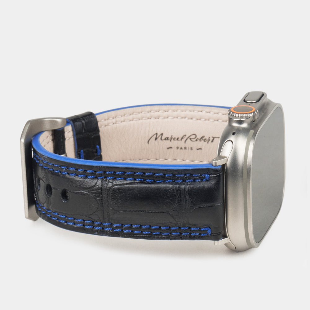Apple Watch Ultra 49 mm aus schwarzem Alligatorleder, Naht und Kante in Blau, mit Adaptern und Schnalle aus Titan | 3/4-Ansicht mit Innenfutter aus Leder und Marcel-Robert-Signatur