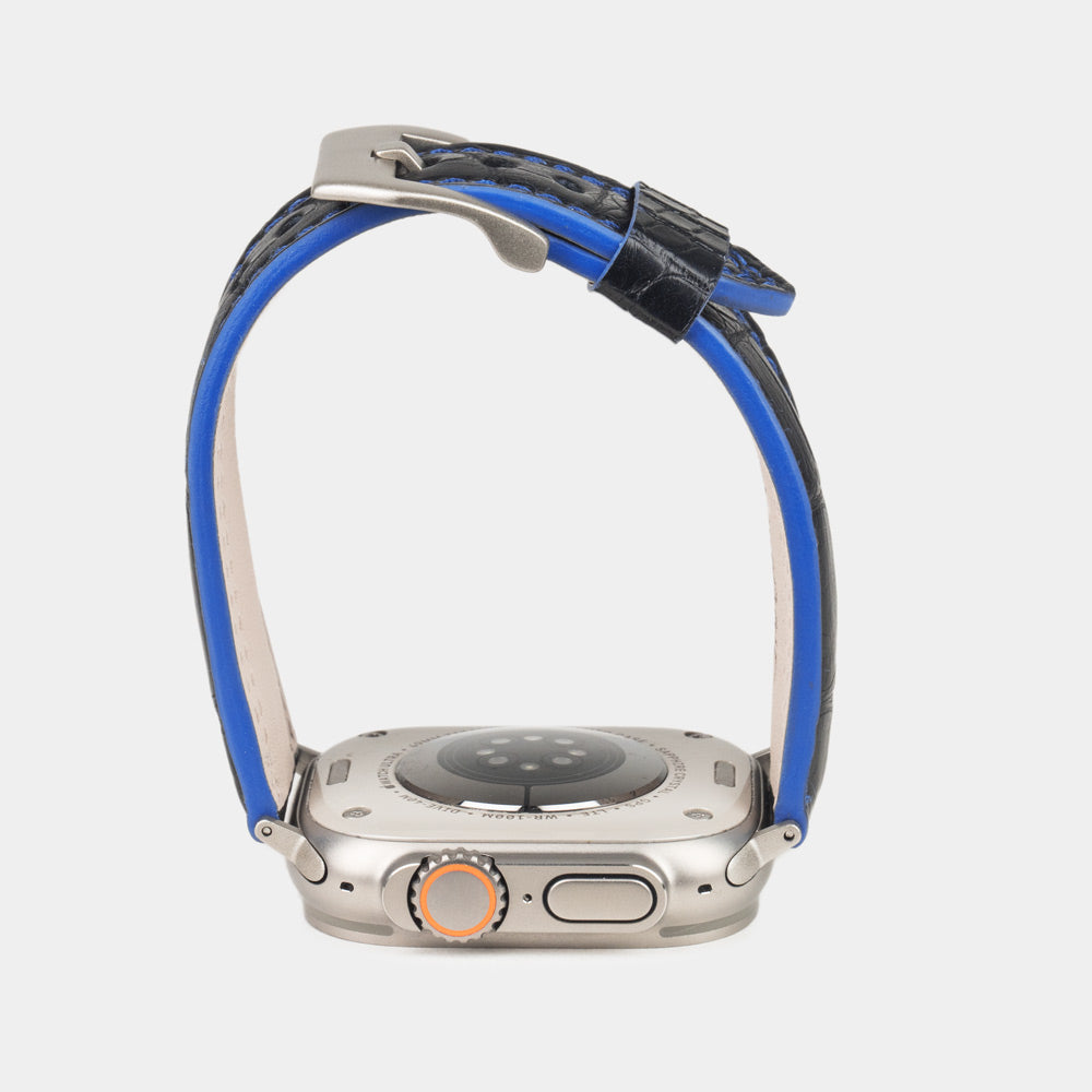 Apple Watch Ultra 49 mm aus schwarzem Alligatorleder, Naht und Kante in Blau, mit Adaptern und Schnalle aus Titan | Gehäuse unten, um die blau gefärbte Kante zu sehen