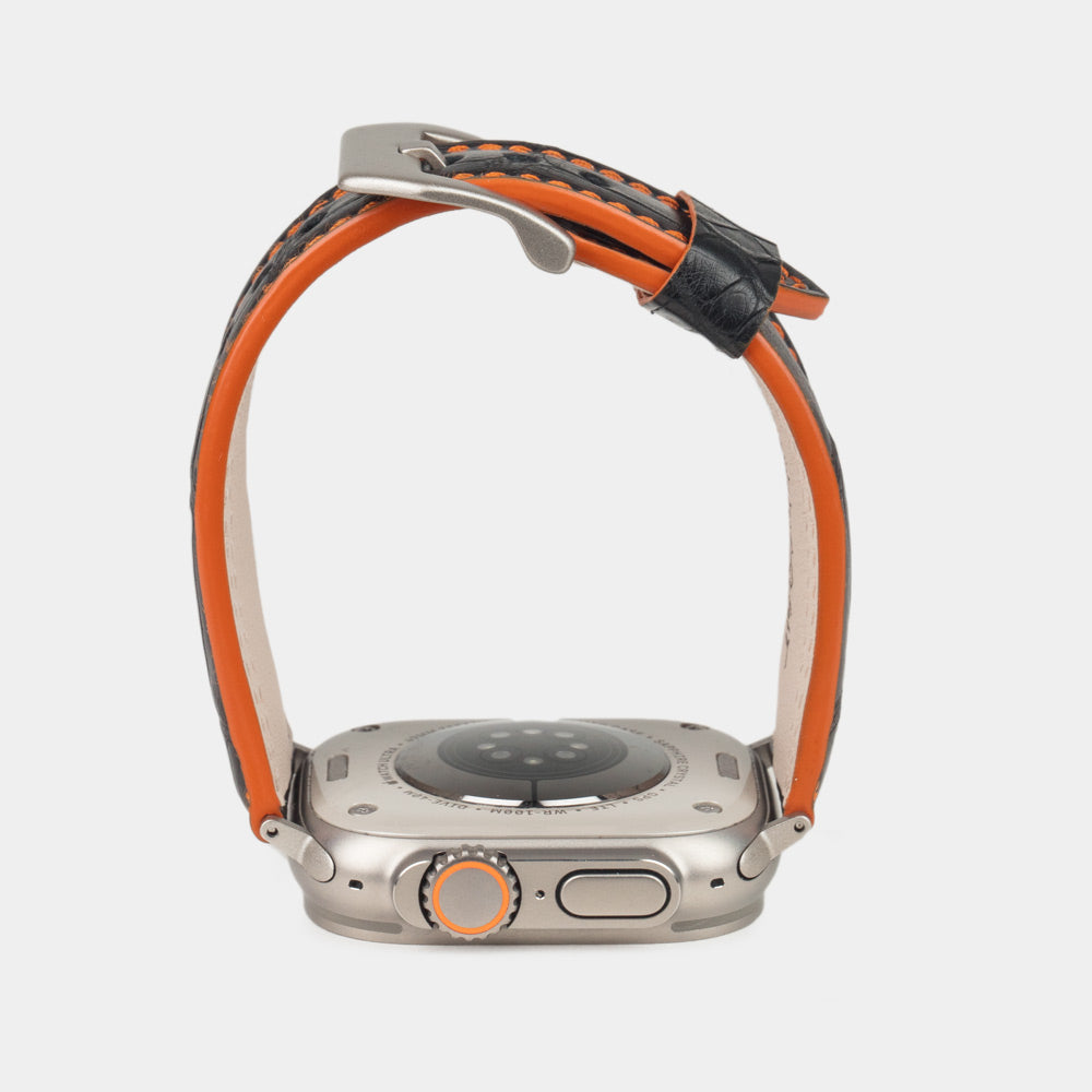 Apple Watch Ultra 49 mm aus schwarzem Alligatorleder, Naht und Kante in Orange, mit Adaptern und Schnalle aus Titan | Gehäuse unten, um die orange gefärbte Kante zu sehen