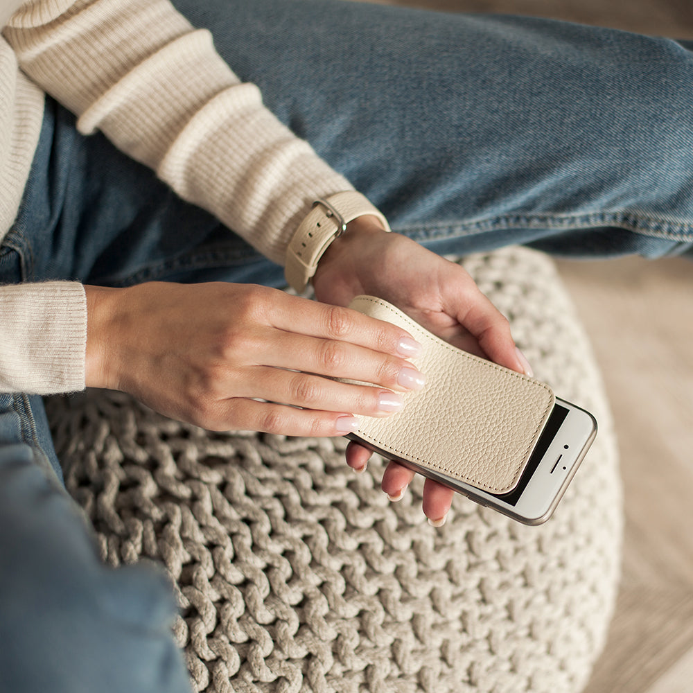 Lederen hoesje Crème voor iPhone SE in de handen van een vrouw, zittend op een gebreide poef