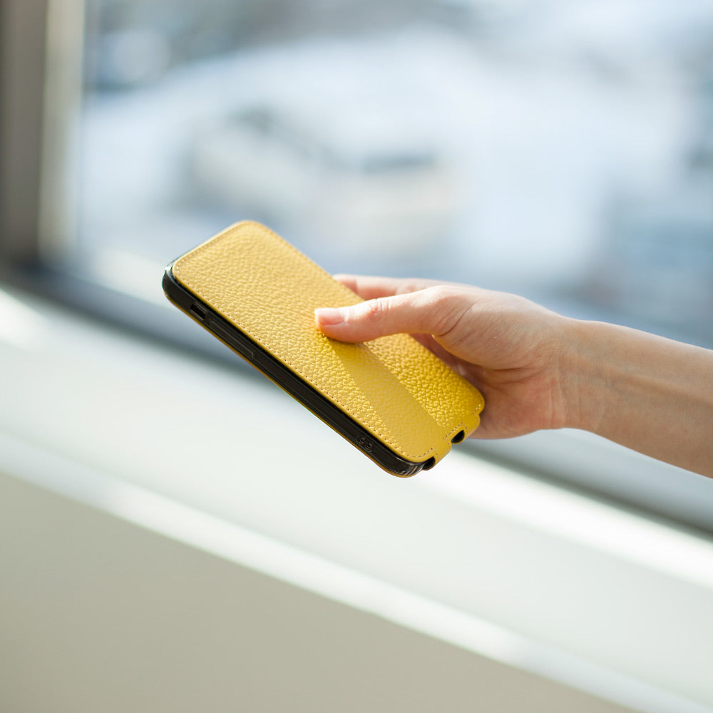 Yellow calfskin leather flip case for iPhone 15 held in one hand, flap closed flat over the screen