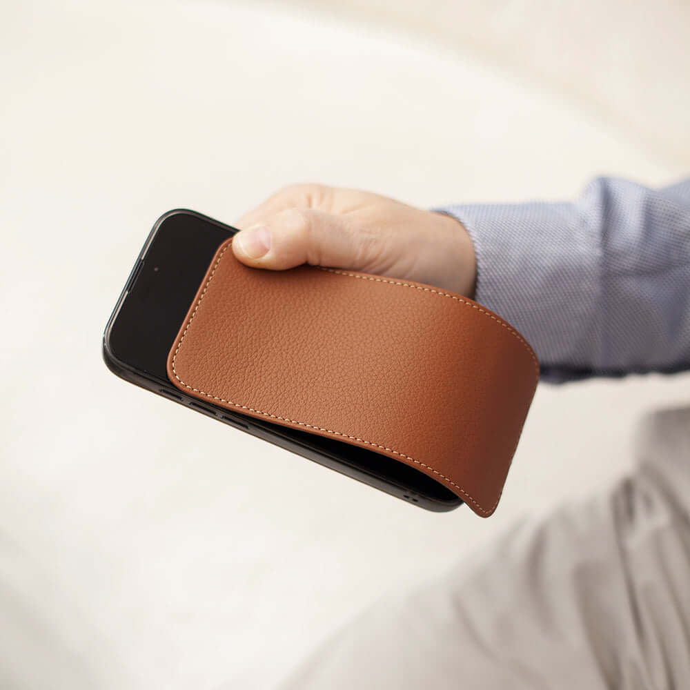 Person holding a smartphone with a brown leather case against a neutral background