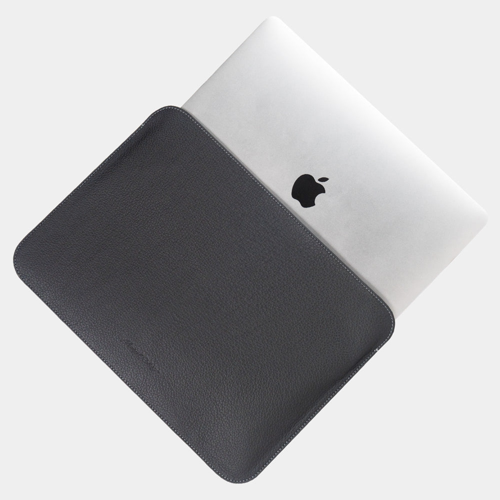 Leren laptophoes 14 inch in zwart, met MacBook deels erin geschoven — slanke minimalistische MacBook hoes