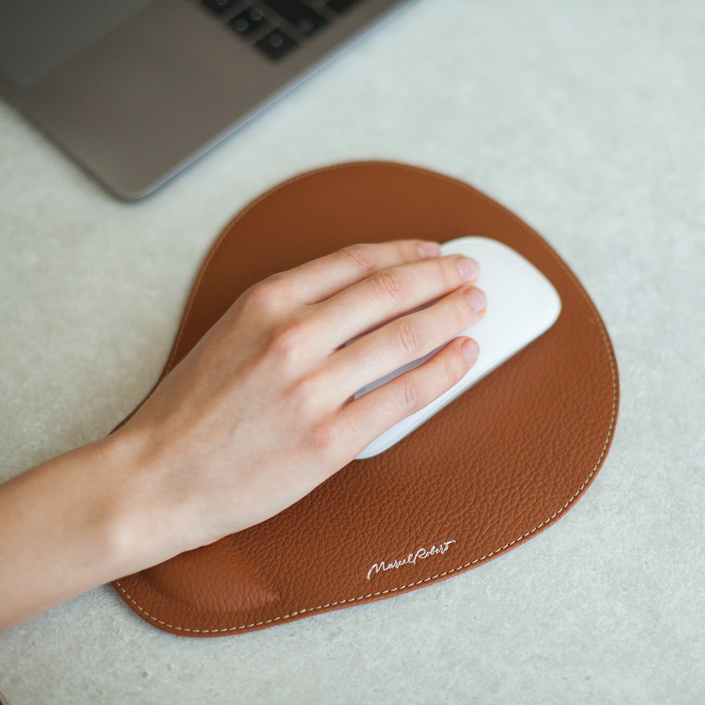Mano sul mouse, tappetino mouse in pelle gold accanto a un portatile