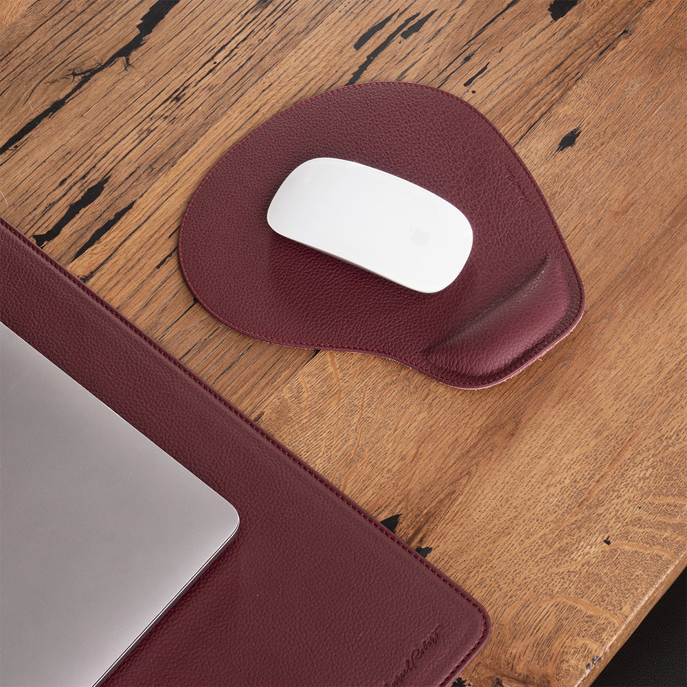 Tappetino mouse in pelle bordeaux con mouse su una scrivania in legno, portatile accanto