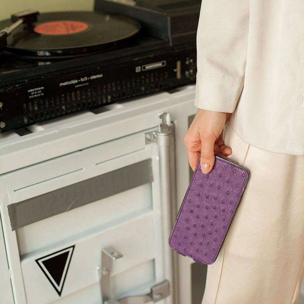 Person holding a phone in ostrich leather case in front of a record player on a white cabinet.