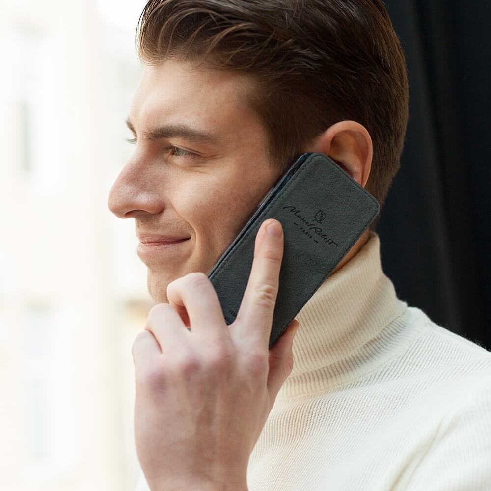 Man holding a phone in leather flip case with a brand logo, smiling outdoors.