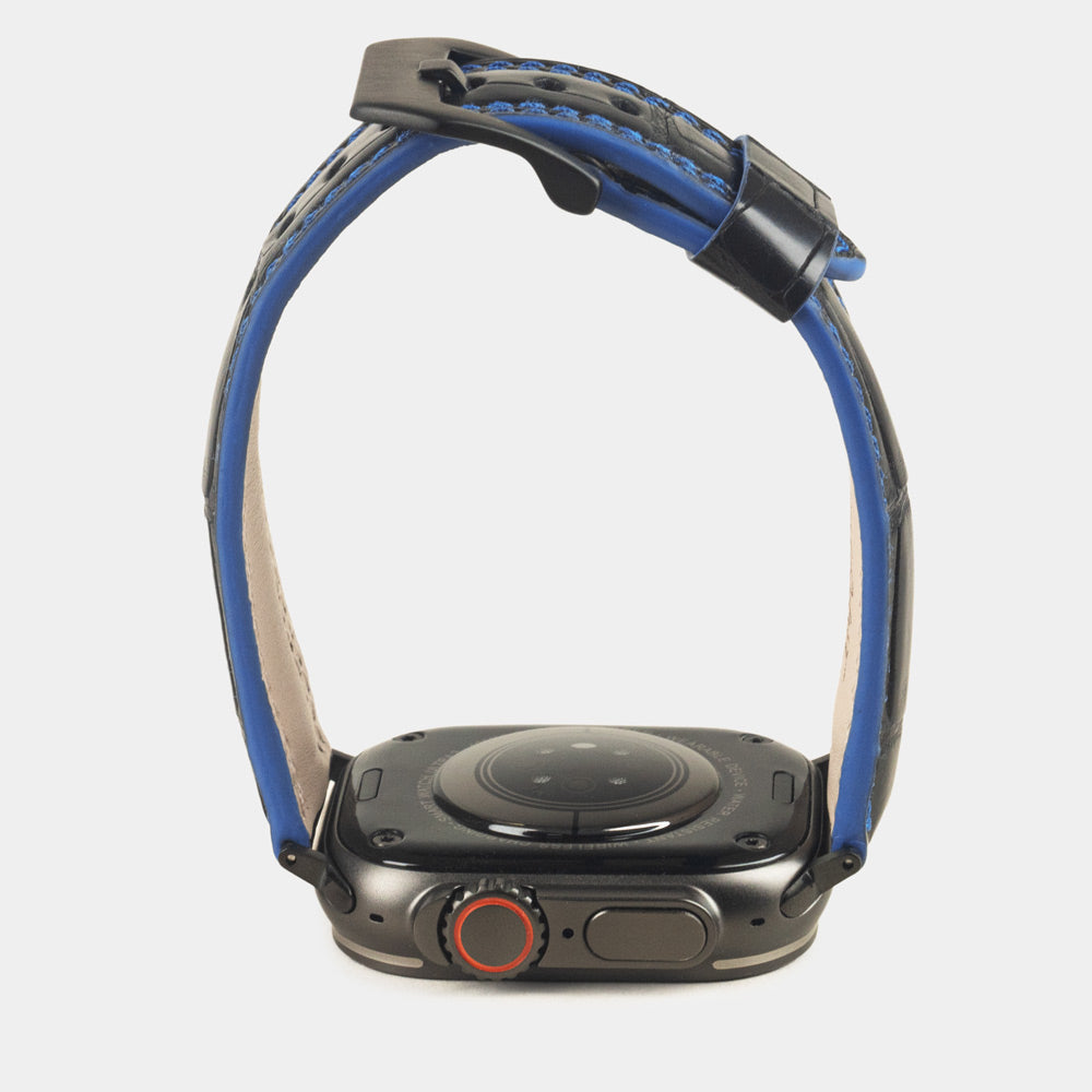 Apple Watch Ultra 49 mm aus schwarzem Alligatorleder, Naht und Kante in Blau, mit schwarzen Adaptern und Schnalle | Gehäuse unten, um das Armbandprofil und die blau gefärbte Kante zu sehen