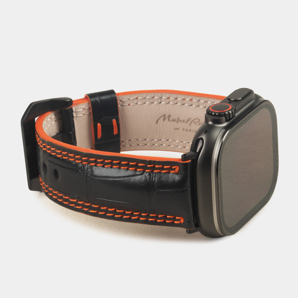 Apple Watch Ultra 49 mm aus schwarzem Alligatorleder, Naht und Kante in Orange, mit schwarzen Adaptern und Schnalle | 3/4-Ansicht mit Innenfutter aus Leder und Marcel-Robert-Signatur