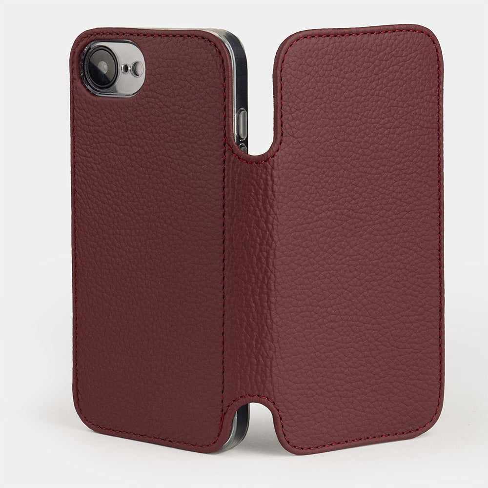 funda folio iPhone 17e & 16e de piel de becerro bordeaux – de pie y abierta, vista exterior que muestra el dorso con el recorte para la cámara única y la tapa frontal desplegada