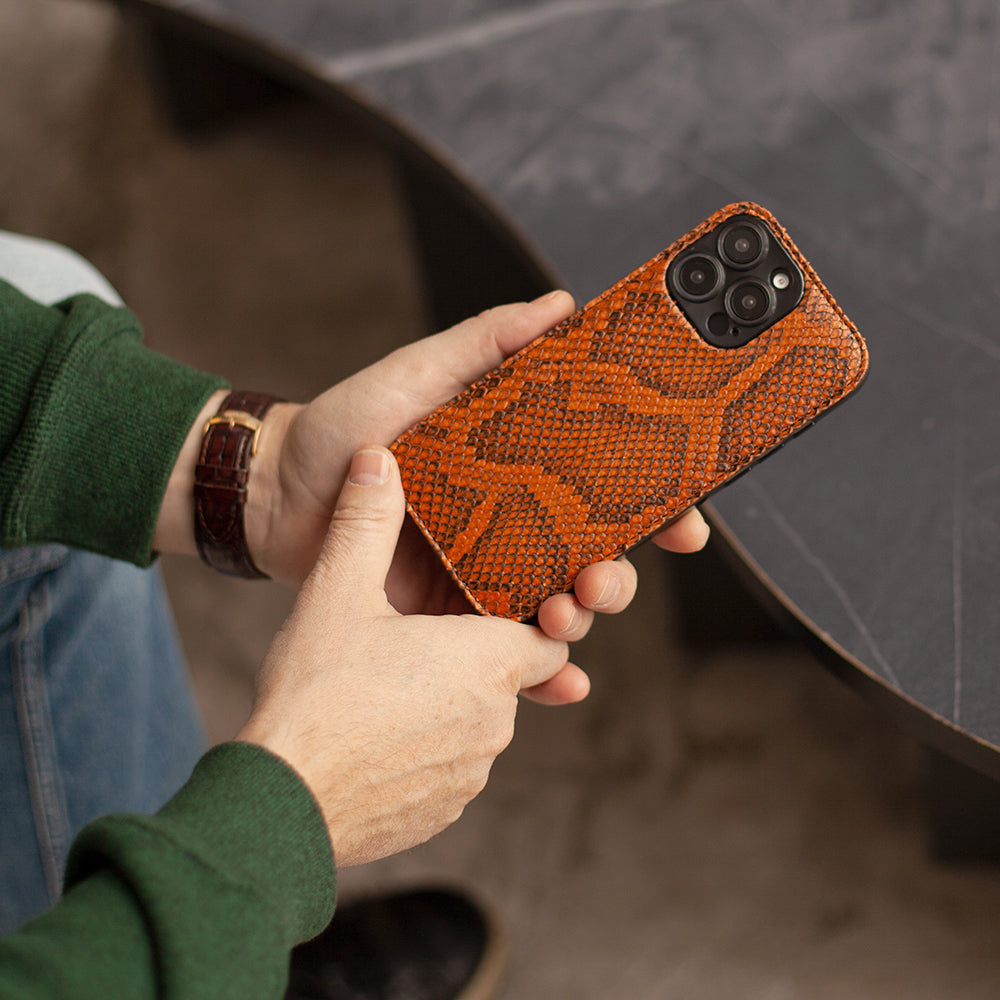 Person holding a phone with an orange snake-textured case against a blurred background