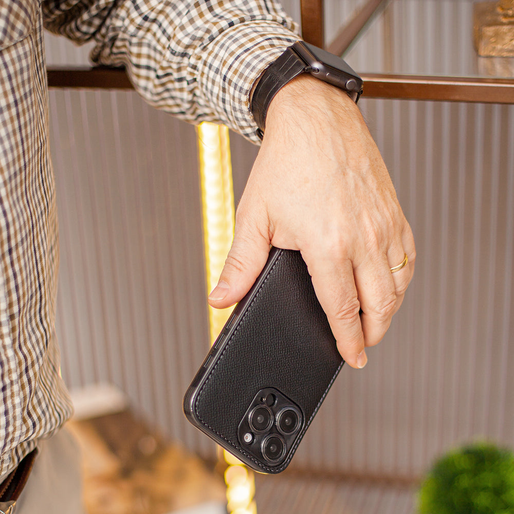 Person holding a phone in black leather case with a blurred indoor background