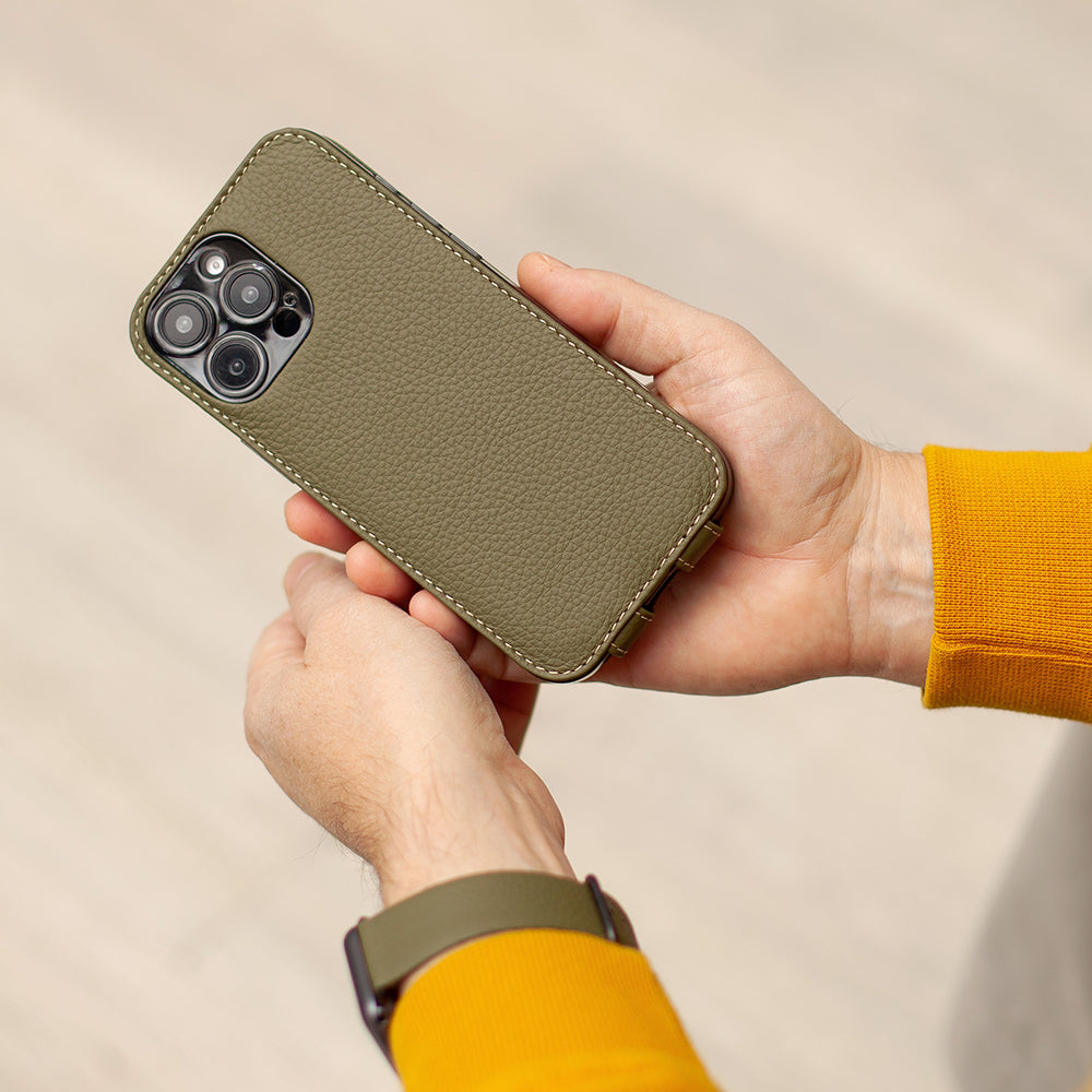 Person holding a green phone in leather case against a beige background