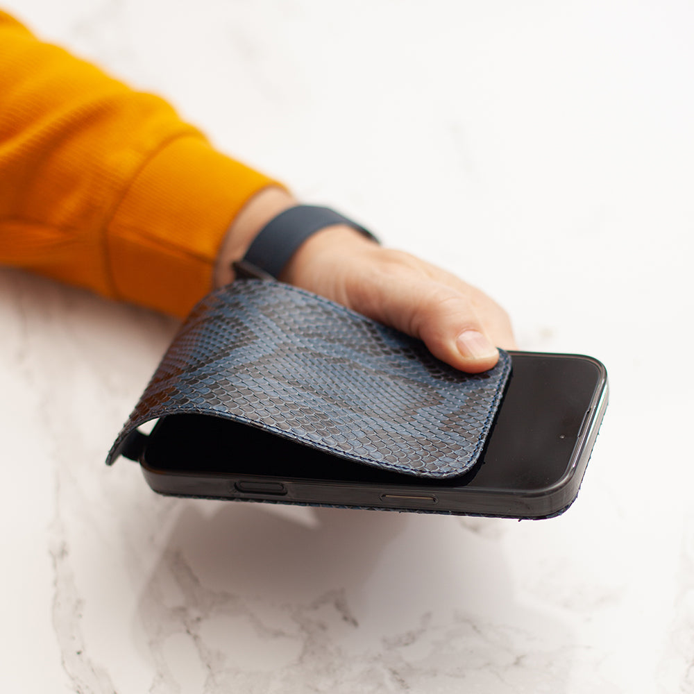 Hand holding a blue python textured phone case over a smartphone on a white marble surface