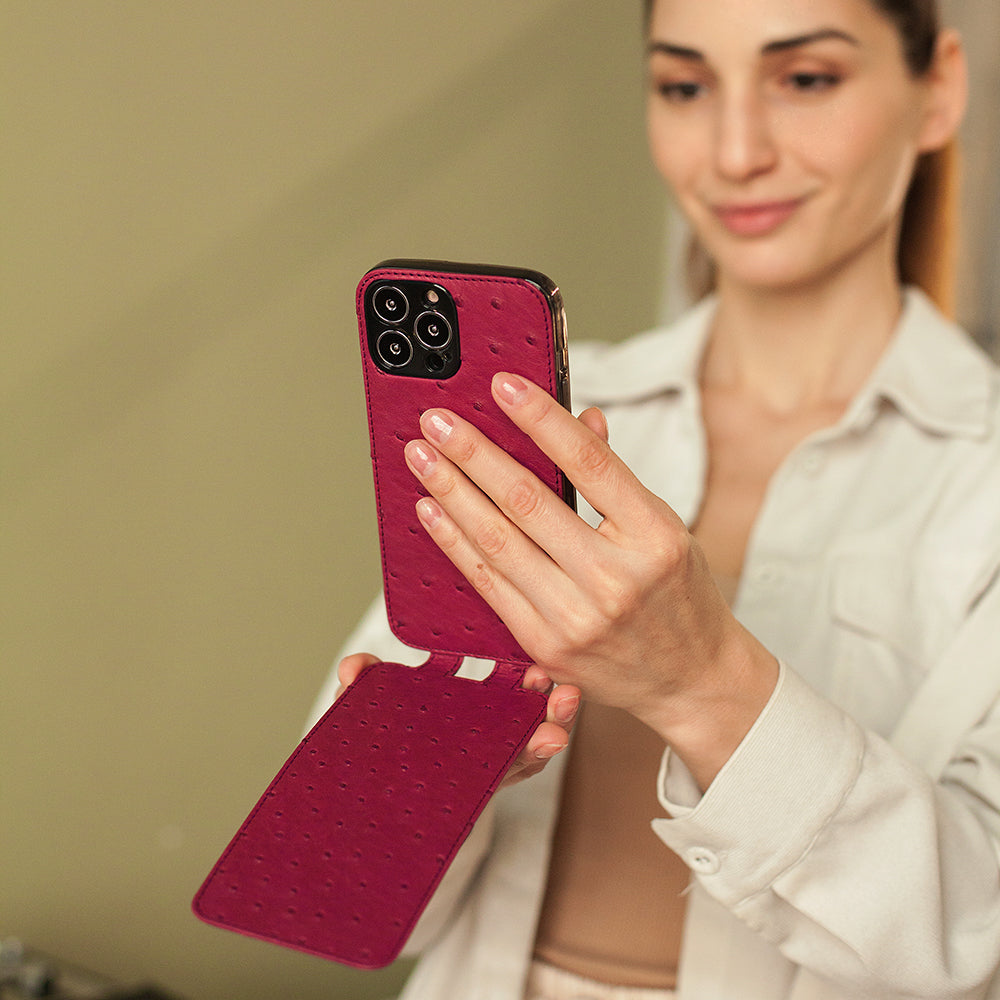 Woman using iPhone 13 Pro with Marcel Robert fuchsia ostrich leather case flap folded behind for hands-free use