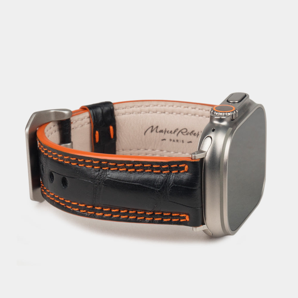 Apple Watch Ultra 49 mm aus schwarzem Alligatorleder, Naht und Kante in Orange, mit Adaptern und Schnalle aus Titan | 3/4-Ansicht mit Innenfutter aus Leder und Marcel-Robert-Signatur