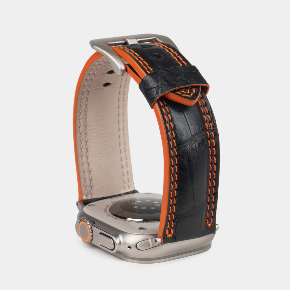 Apple Watch Ultra 49 mm aus schwarzem Alligatorleder, Naht und Kante in Orange, mit Adaptern und Schnalle aus Titan | Nahaufnahme der quadratischen Schuppen und der Doppelnaht in Orange