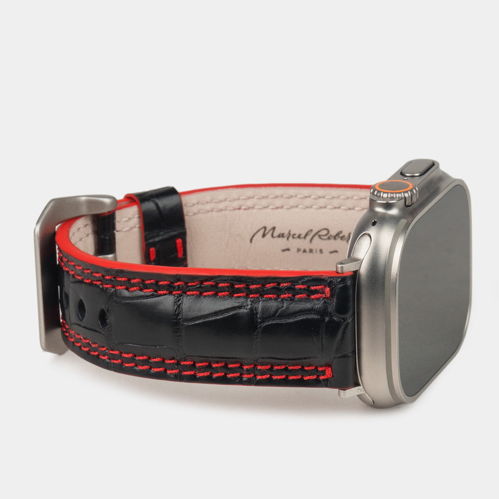 Apple Watch Ultra 49 mm aus schwarzem Alligatorleder, Naht und Kante in Rot, mit Adaptern und Schnalle aus Titan | 3/4-Ansicht mit Innenfutter aus Leder und Marcel-Robert-Signatur