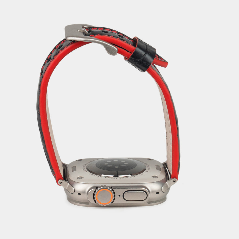 Apple Watch Ultra 49 mm aus schwarzem Alligatorleder, Naht und Kante in Rot, mit Adaptern und Schnalle aus Titan | Gehäuse unten, um die rot gefärbte Kante zu sehen