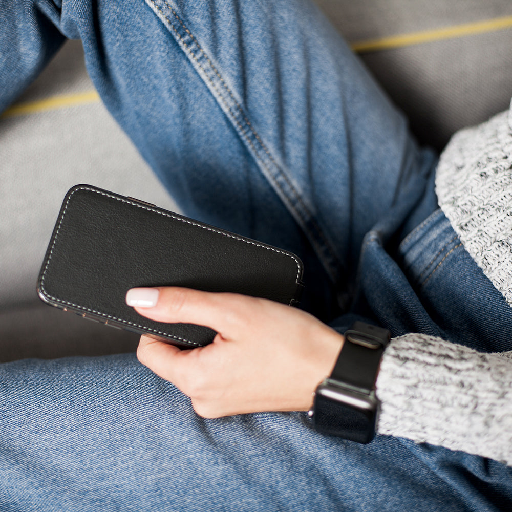 Funda de piel Negro para iPhone SE en la mano de una mujer, sentada con las piernas cruzadas