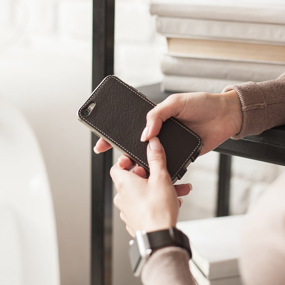 Funda de piel Marrón para iPhone SE en las manos de una mujer, cerca de una estantería