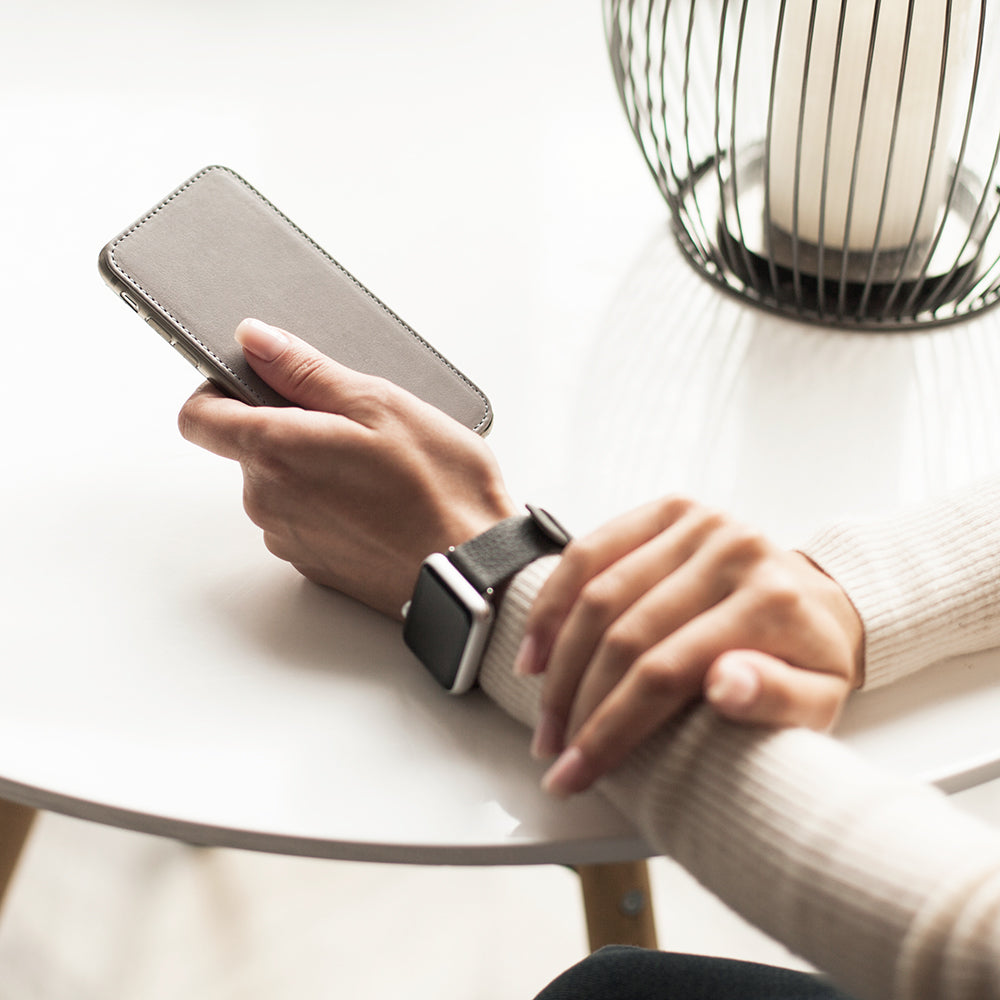 Funda de piel Gris Piedra para iPhone SE en la mano de una mujer, en una mesa