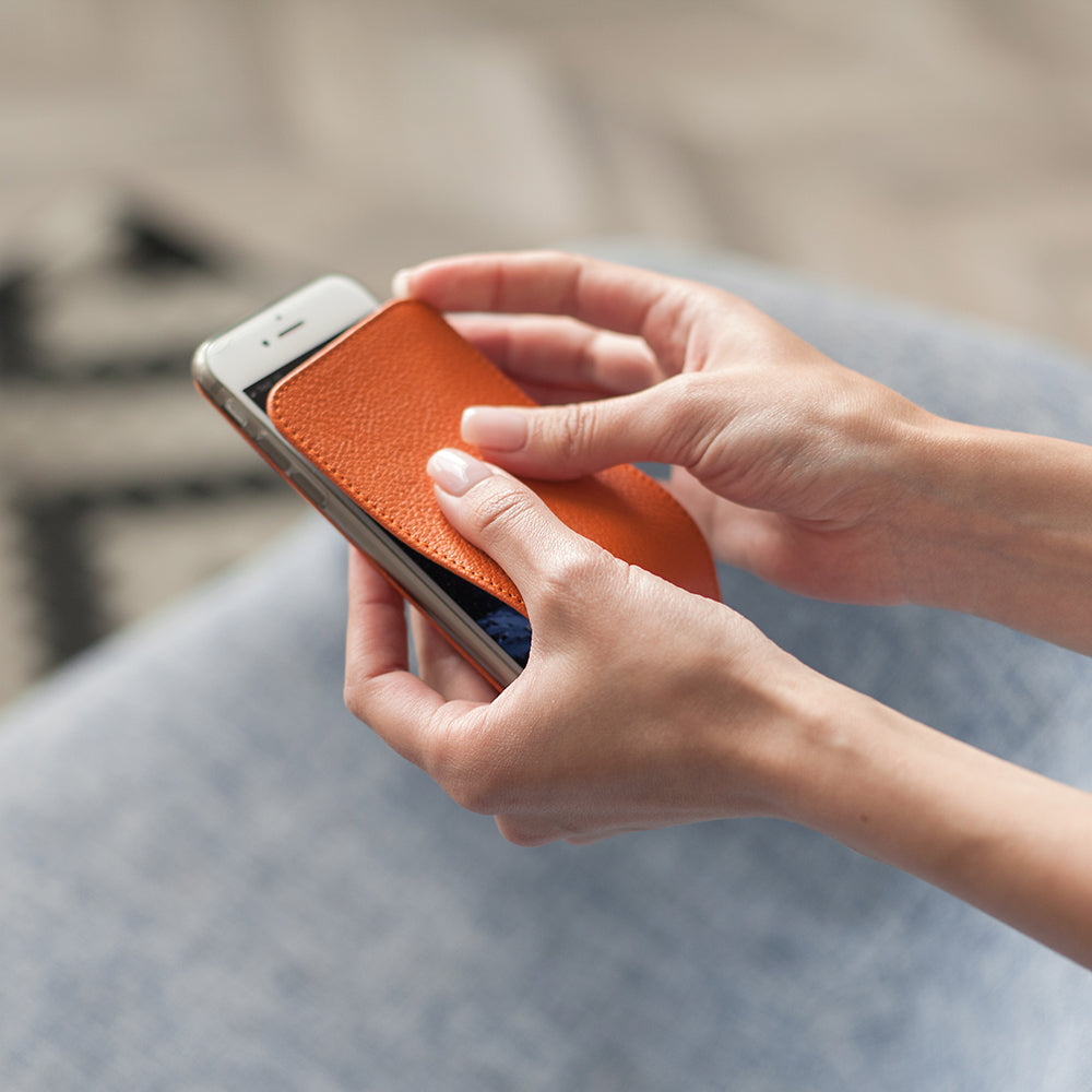 Funda de piel Naranja para iPhone SE en las manos de una mujer, insertando el smartphone en la funda