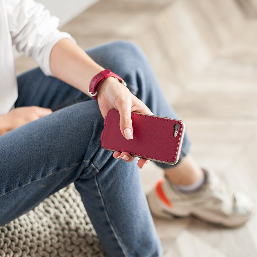 Funda de piel Fucsia para iPhone SE en la mano de una mujer, sentada con las piernas cruzadas