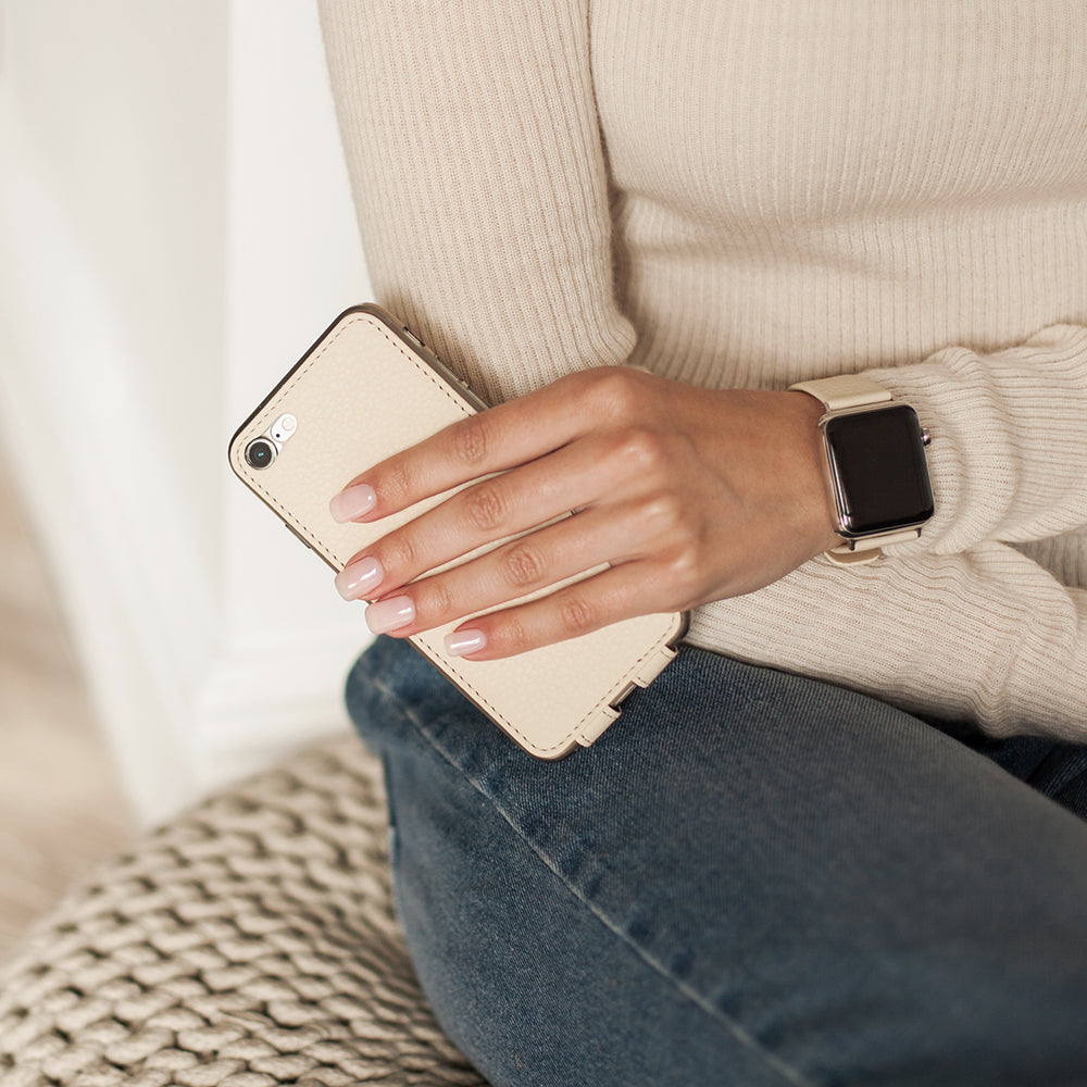 Funda de piel Crema para iPhone SE en la mano de una mujer, sostenida contra su jersey
