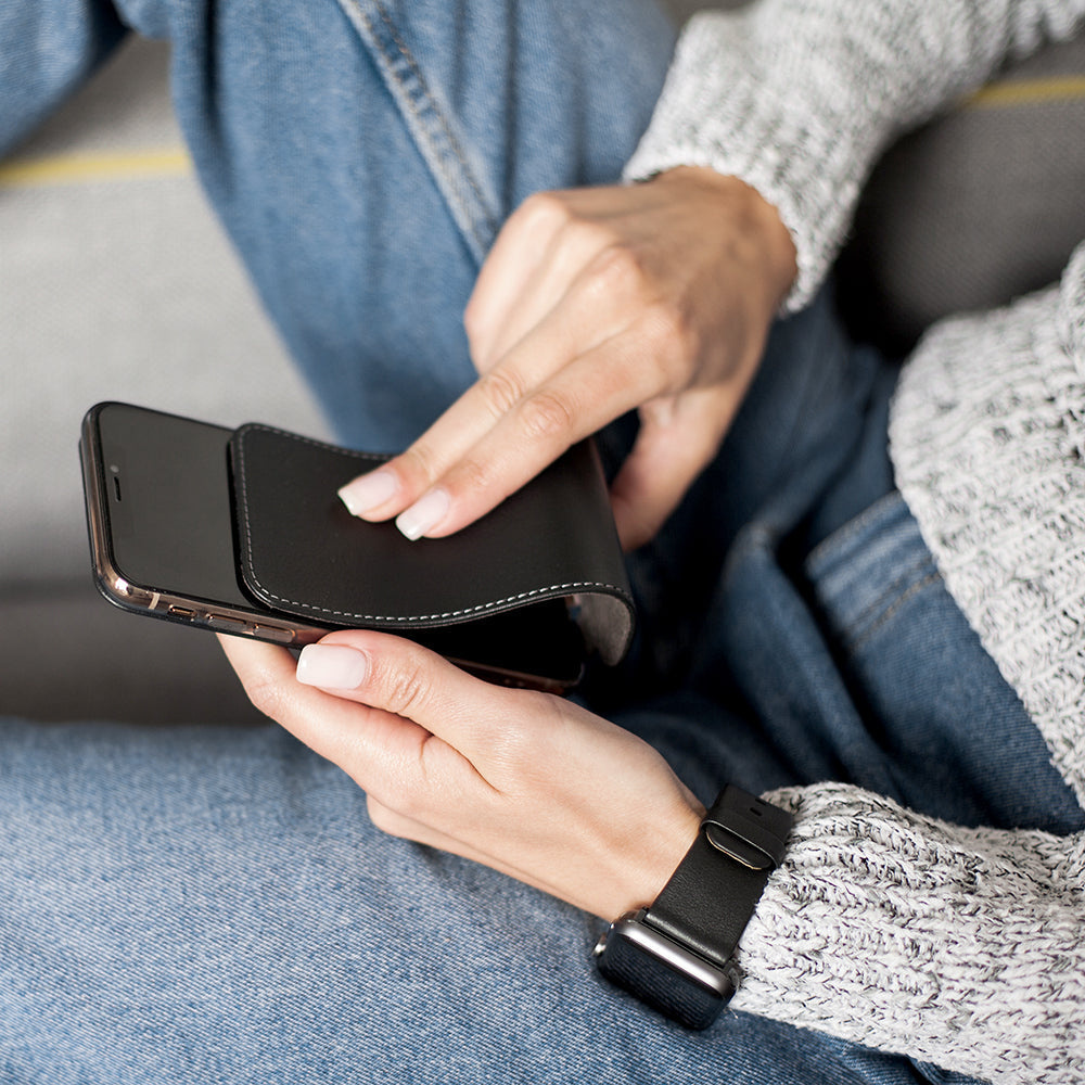 Black leather case for iPhone X in woman's hands, folding the cover to clean the phone screen