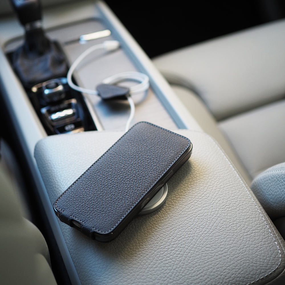 Black calfskin leather flip case for iPhone 15 resting closed on a car centre console