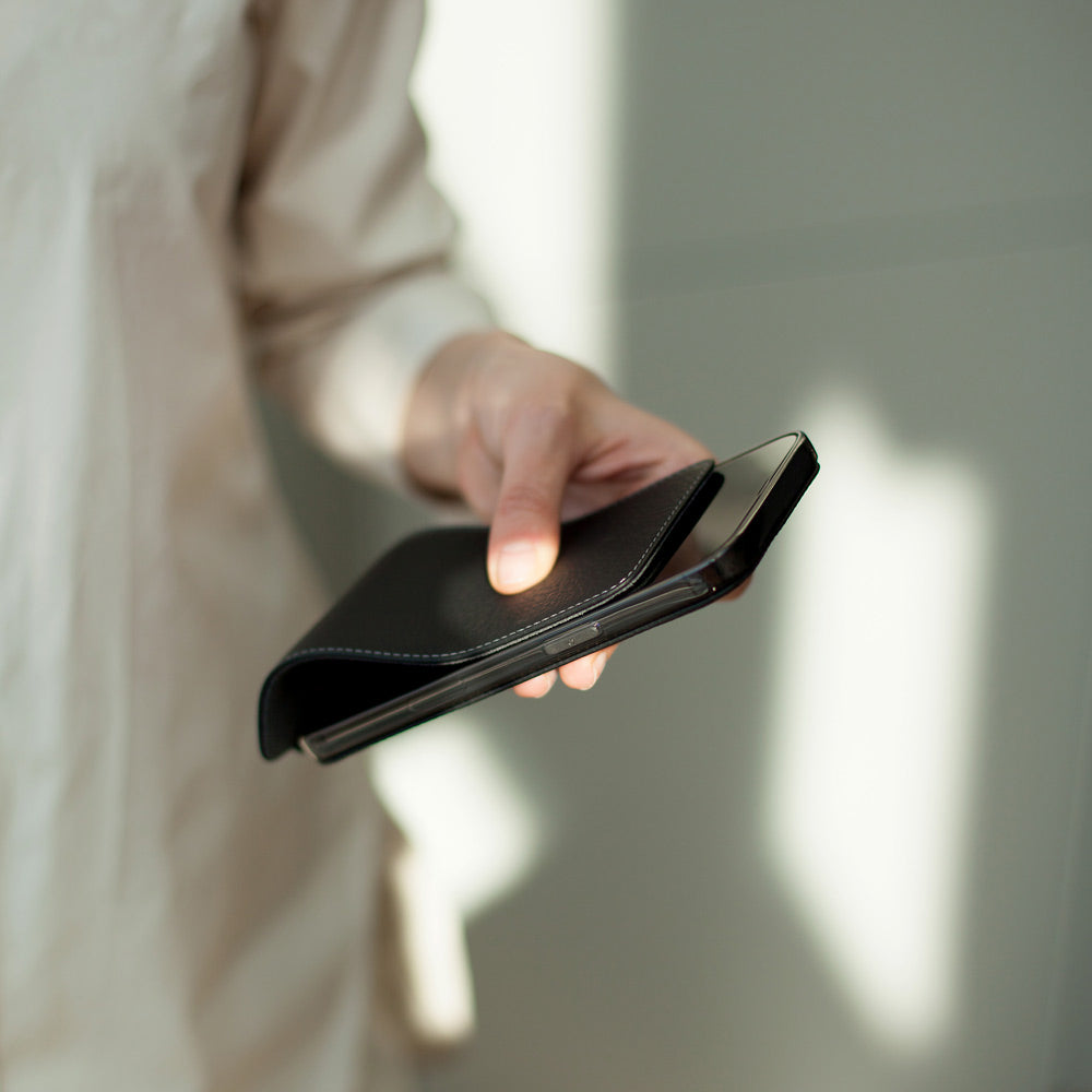 Black calfskin leather flip case for iPhone 15 held in one hand, flap folded open behind the phone