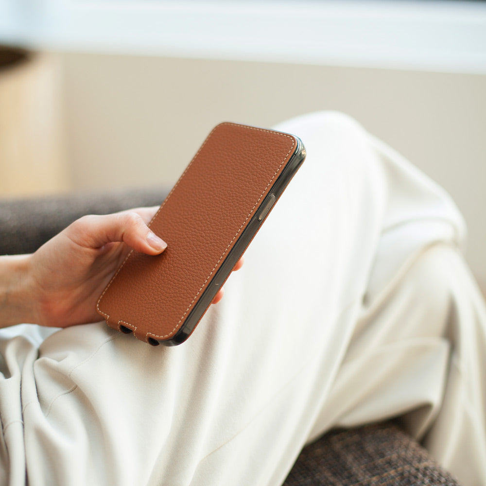 Gold calfskin leather flip case for iPhone 15 held in one hand, flap closed flat over the screen