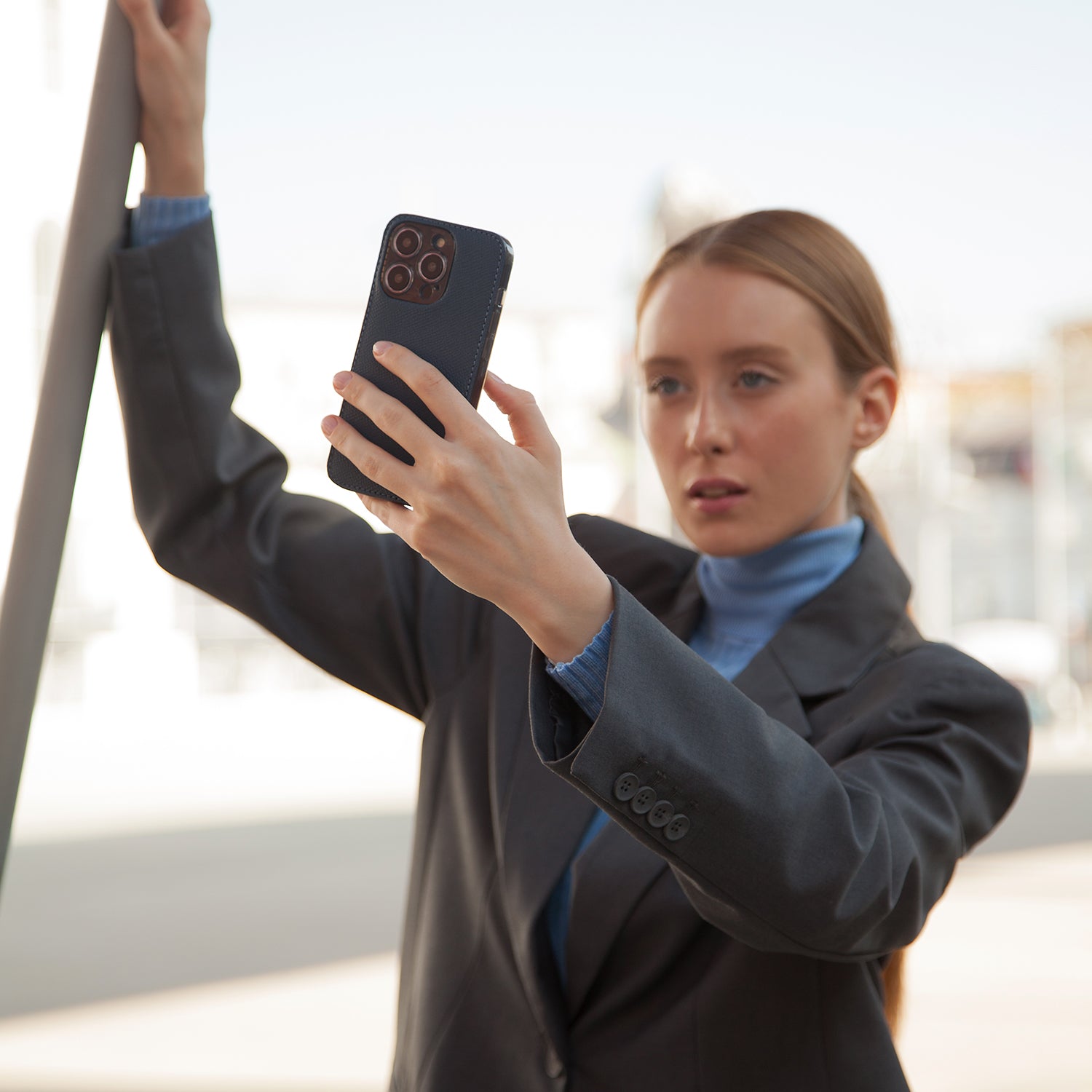 Blonde woman in business attire taking a photo with iPhone 15 Pro in Marcel Robert black Saffiano calfskin leather case