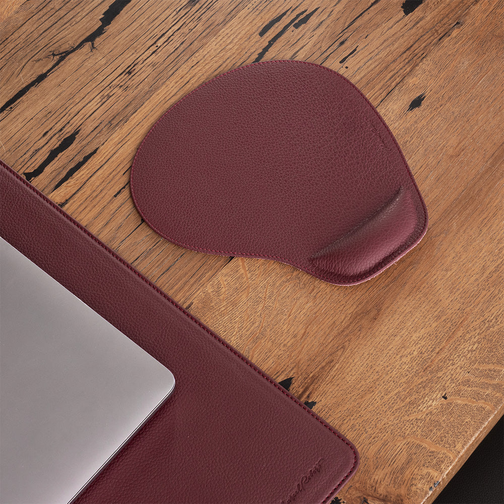 Tappetino mouse in pelle bordeaux su una scrivania in legno, accanto a un portatile